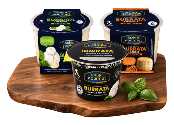 Tres burratas Spiga Gourmet sobre una tabla de madera: la clásica delante y, detrás, la selezione al pesto y la affumicata, con hojas de albahaca al lado