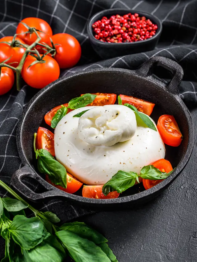 Burrata en sartén de hierro, rodeada de tomate en cuartos y hojas de albahaca